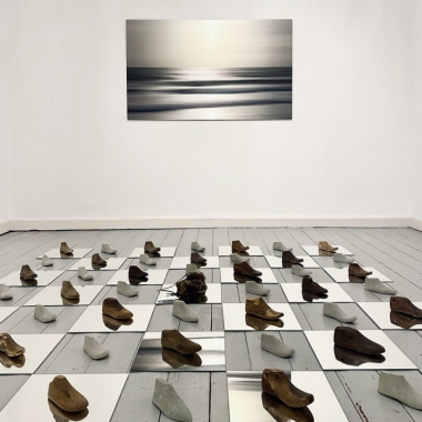 Installation on the floor with mirror tiles organized like a chess field with shoe objects , casted from concrete and old shoe lasts for children